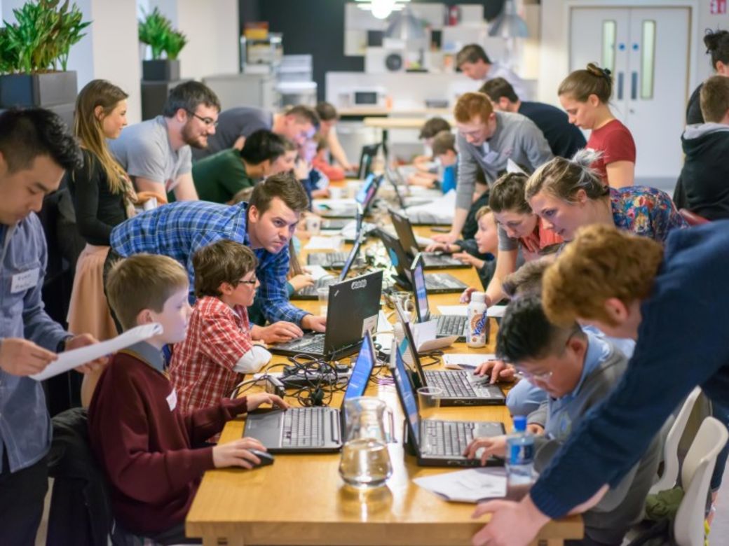 Foto van mensen en kinderen aan een lange tafels, werkend aan laptops