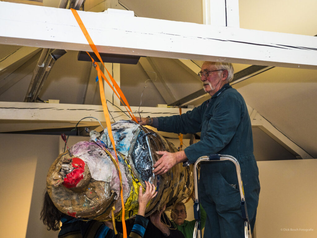 Kunstenaar Nol die een kunstwerk bevestigd aan een balk van de zolder van het Gorcums Museum